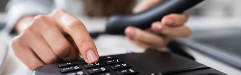 Eine Hand bedient ein Tastentelefon, die andere Hand hält einen Telefonhörer