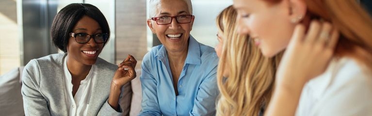 Vier Frauen sitzen an einem Tisch, eine von ihnen hat ein Notebook vor sich stehen