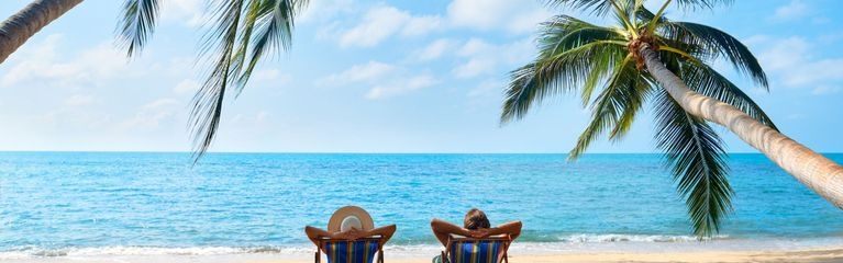 Strand mit Palmen und zwei Personen im Liegestuhl