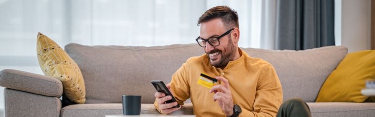 Ein Mann hält in einer Hand eine Kreditkarte und in der anderen Hand ein Smartphone