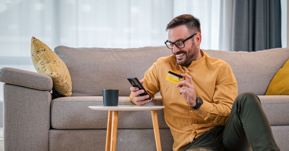 Ein Mann hält in einer Hand eine Kreditkarte und in der anderen Hand ein Smartphone