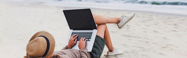 Person mit Laptop am Strand