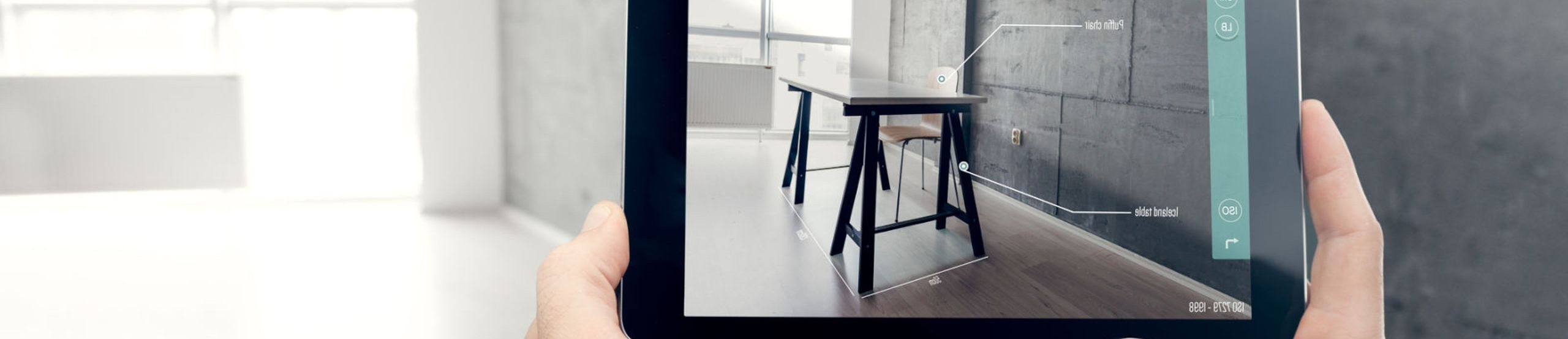 POV: Zwei Hände halten ein Tablet, die App auf dem Display zeigt Möbel im Raum, der in der Realität leer ist