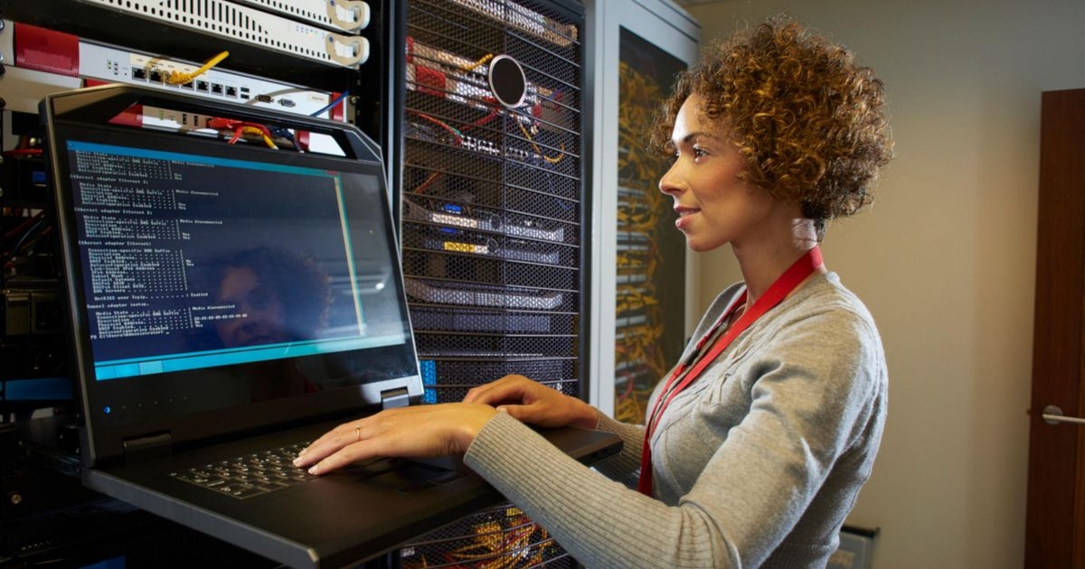 Ein sicheres internes Firmennetzwerk einrichten: Wichtige Tipps Eine Frau steht neben einem Serverschrank und blickt auf ein Laptop. Auf dessen Display ist Code zu sehen