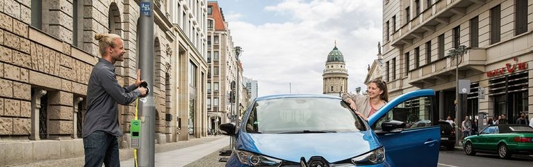  Mann steckt Stecker von seinem blauen Auto in Ubitricity-Ladelösung an einer Straßenlaterne