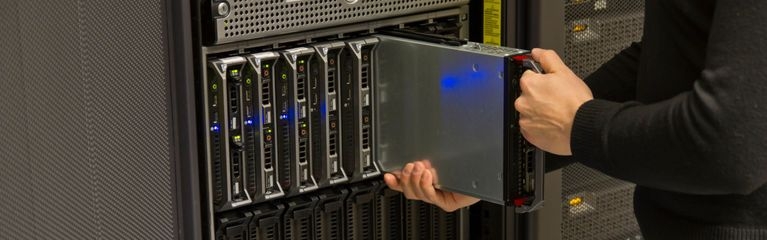 Eine Person steht vor einem Serverschrank und schiebt eine einzelne Server Blade in das entsprechende Blade-Gehäuse.