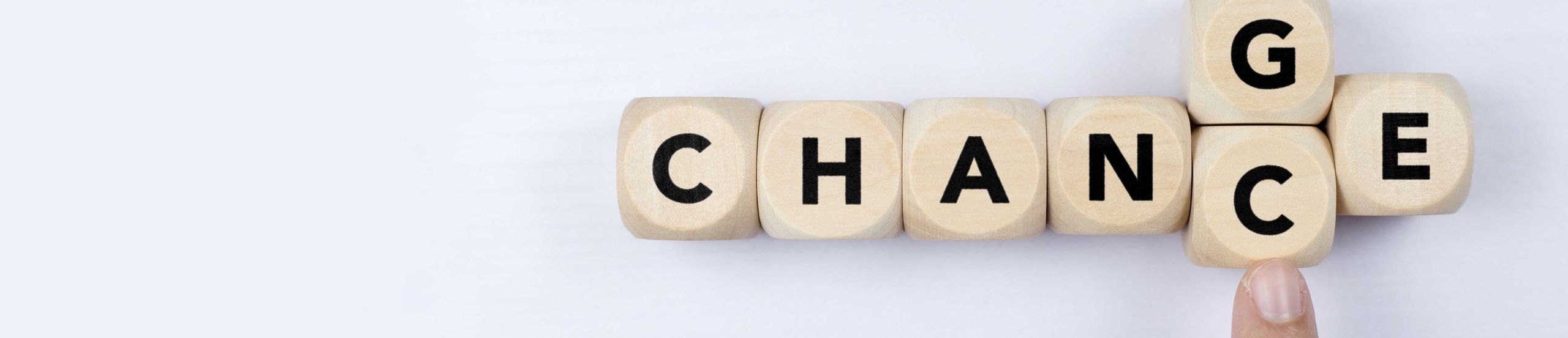 Mehrere Buchstabenwürfel, die zusammen das Wort Change ergeben. Ein Finger schiebt von unten ein C an die Stelle des G, sodass aus Change das Wort Chance wird.