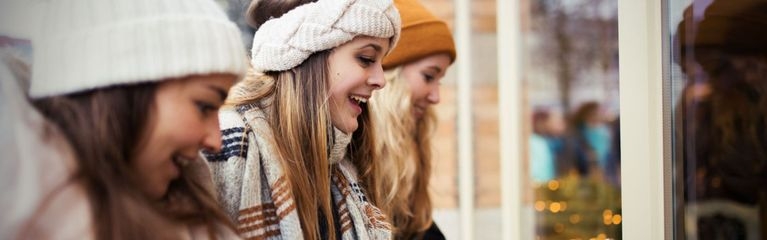 Frauen mit Mützen und Schals bekleidet schauen begeistert auf ein Schaufenster