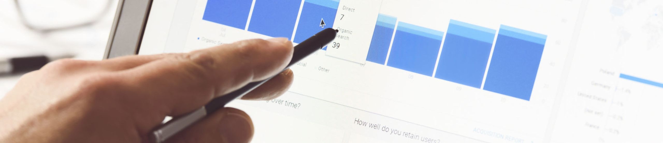 Eine Hand hält einen Stift vor das Display eines Notebooks mit einem Screenshot der Google Analytics-Auswertung