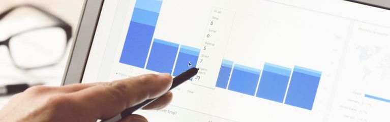 Eine Hand hält einen Stift vor das Display eines Notebooks mit einem Screenshot der Google Analytics-Auswertung