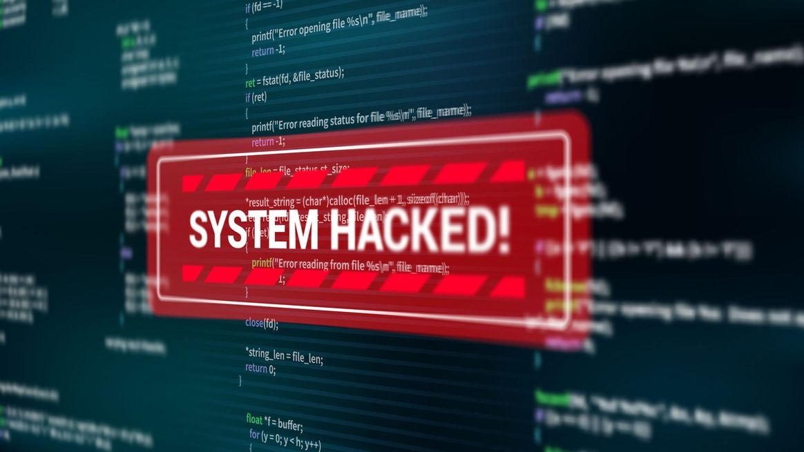 Ein rotes Symbol mit dem Hinweis auf ein gehacktes System befindet sich auf einer Monitoroberfläche. Im Hintergrund ist Programmiercode zu sehen.