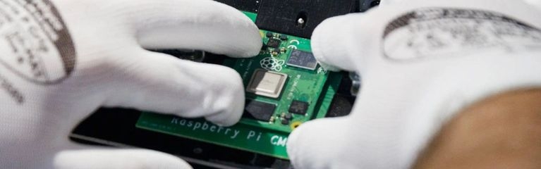 Zwei Hände in antistatischen Handschuhen setzen die Platine eines Raspberry Pi CM in ein anderes Gerät ein.