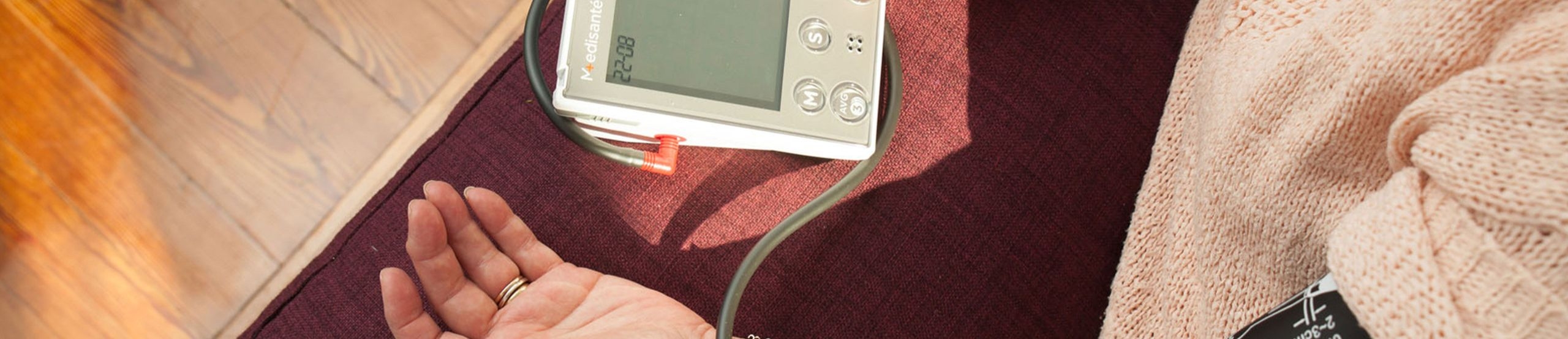 Eine Person hat den linken Arm mit einem Blutdruckmessgerät verbunden und betätigt mit der rechten Hand eine Taste auf diesem Gerät.