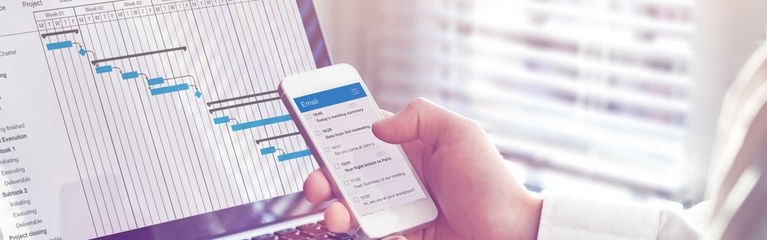 Person arbeitet mit Smartphone am Laptop, auf dem Bildschirm eine Projektmanagement-Software