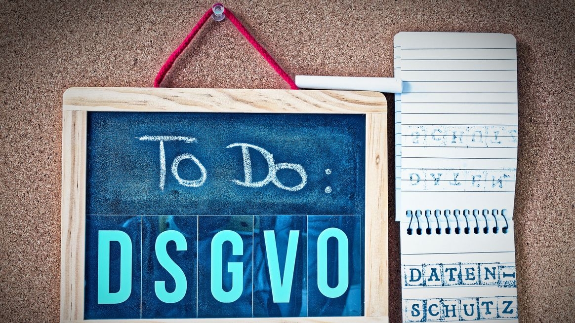 Auf einer Pinwand eine Kreidetafel mit der Beschriftung „ToDo: DSGVO“ und daneben ein Notizblock mit den aufgestempelten Begriffen „Datenschutz“ und „DSGVO“