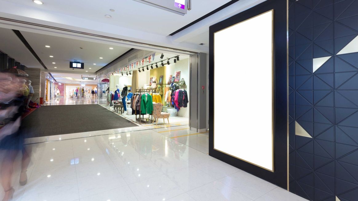 Der Gang in einem Einkaufszentrum mit der Auslage eines Bekleidungsgeschäfts und einem großen weißen Display anstelle eines Schaufensters