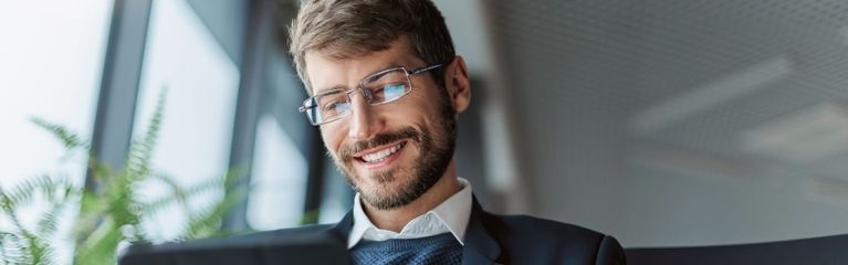 Ein Geschäftsmann im dunklen Anzug und mit Brille schaut auf ein Tablet