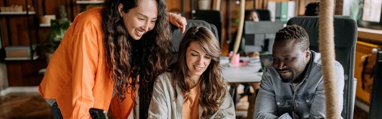 Zwei Frauen und ein Mann gucken in einem hellen Büro zusammen auf einen Bildschirm