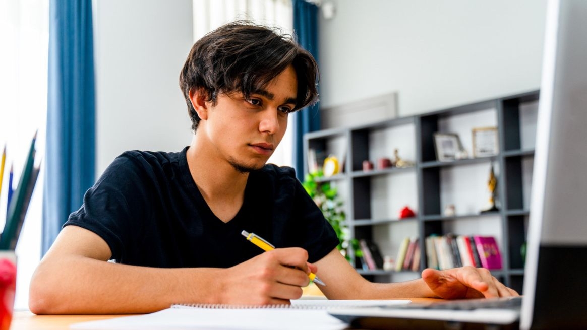 Ein junger Mann sitzt vor seinem Notebook mit einem Stift in der Hand