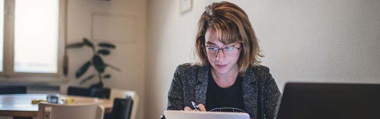 Frau sitzt am Tisch und schaut auf ein Tablet