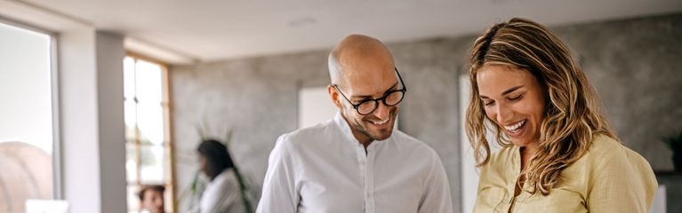 Ein Mann und eine Frau stehen nebeneinander. Der Mann hält ein Tablet in der Hand, die Frau ein Smartphone, auf das beide blicken.