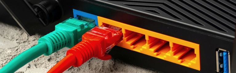 Rückseite eines WLAN-Routers mit WAN- und LAN-Anschlüssen. Ein grünes Ethernet-Kabel steckt im WAN-Anschluss, ein rotes Ethernetkabel steckt in einem LAN-Anschluss.