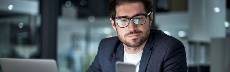 Mann guckt auf sein Smartphone, das Display spiegelt sich in seiner Brille