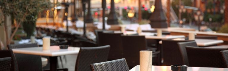 Leere Tische und Stühle auf einer Terrasse. Darauf stehen Kerzen und Aschenbecher