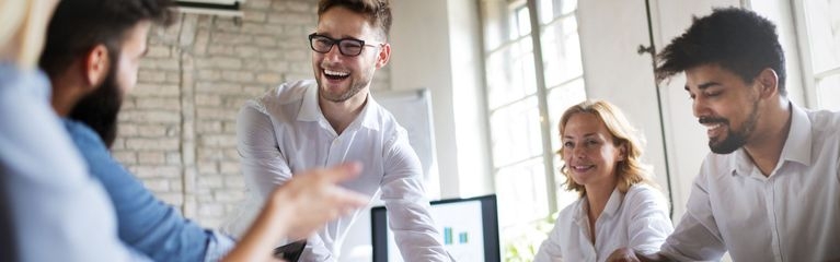 Drei junge Männer und zwei Frauen sitzen und stehen um einen Tisch herum und lachen