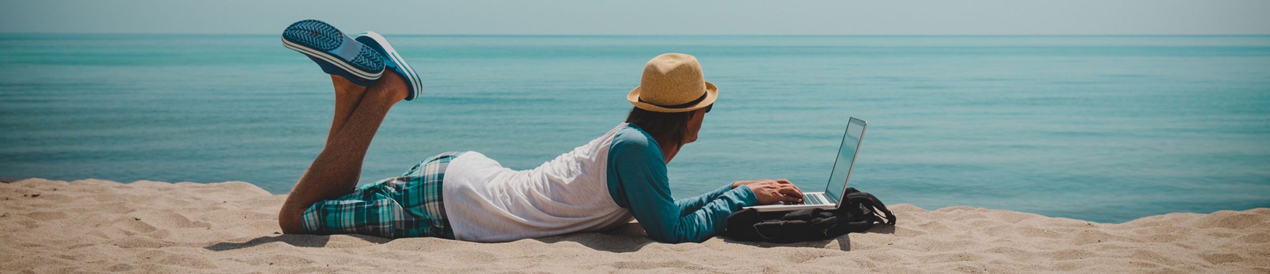 Mann liegt am Strand mit Laptop und schaut aufs Meer