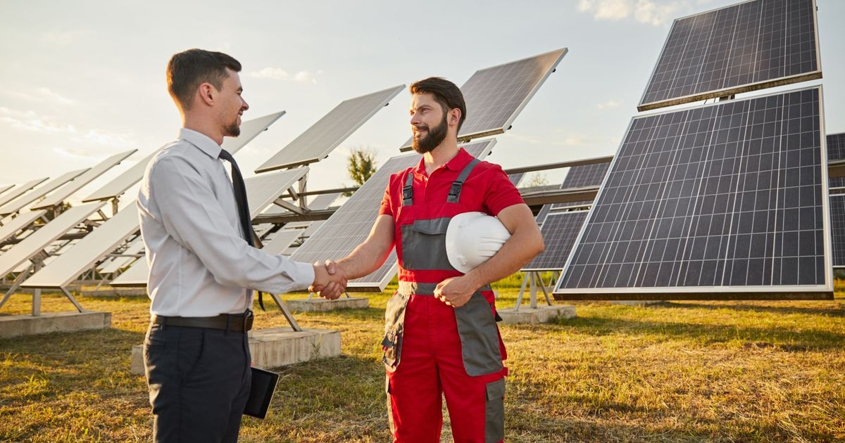 Geschäftsmann schüttelt die Hand eines Ingenieurs vor Solaranlage.