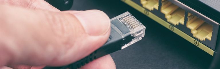 Hand, die einen Ethernet-Netzwerkstecker in einen Internetrouter steckt.