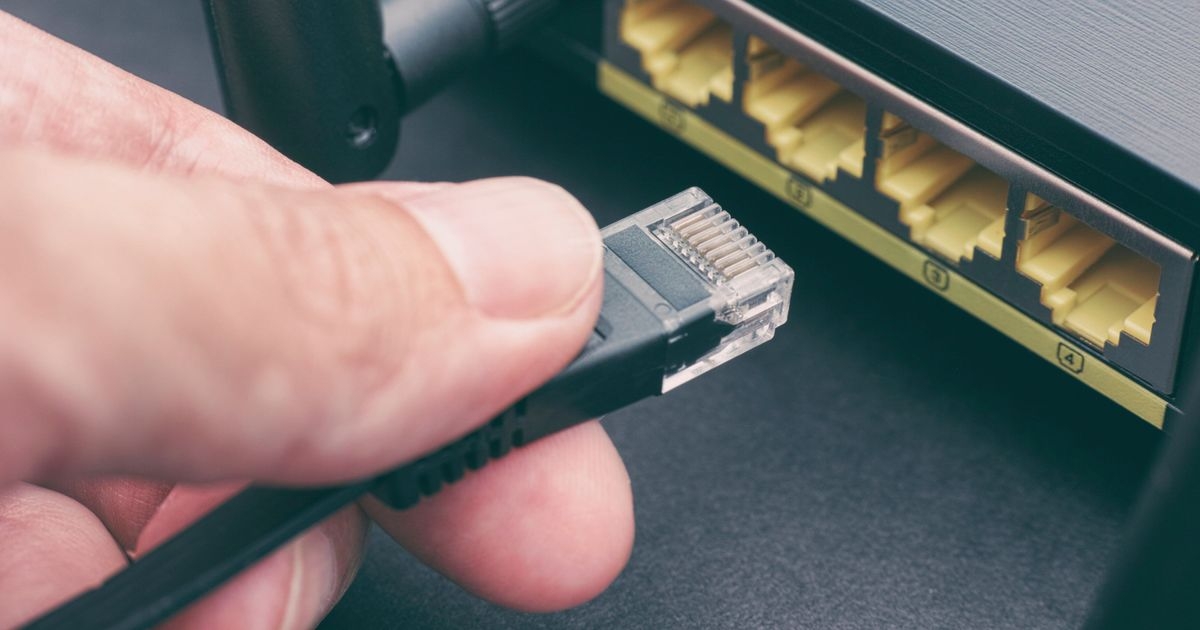 Hand, die einen Ethernet-Netzwerkstecker in einen Internetrouter steckt.