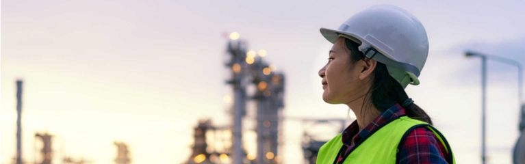 Eine Frau steht mit einem Notebook in der Hand vor einer Industrieanlage.