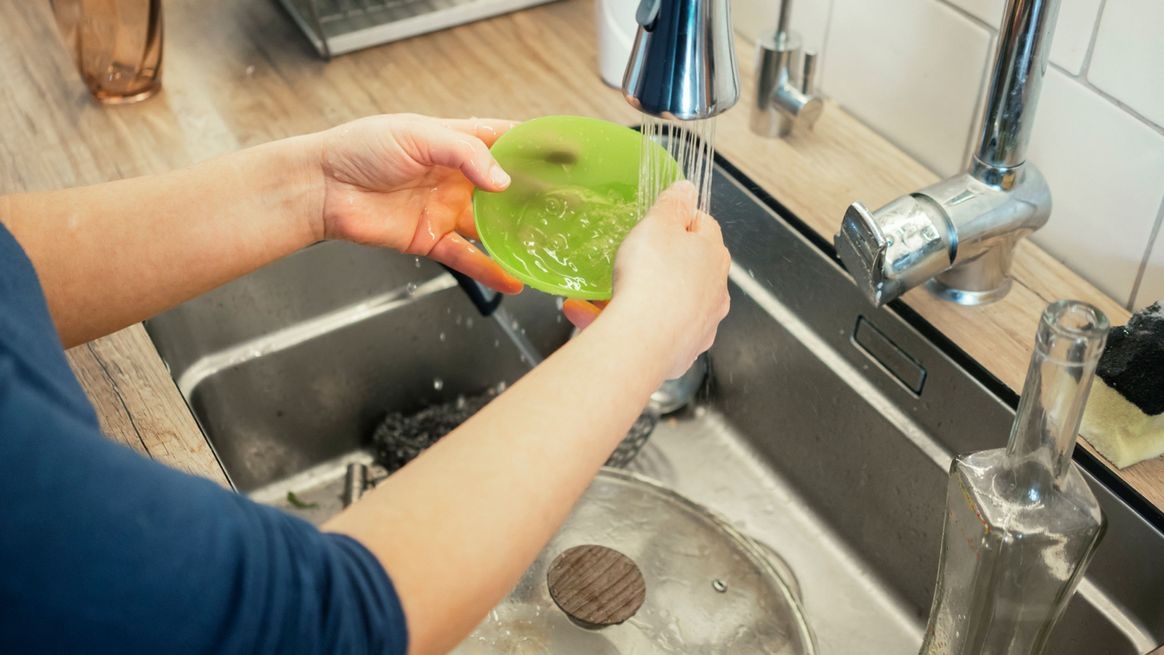Person wäscht eine Plastikschale an einem Waschbecken ab