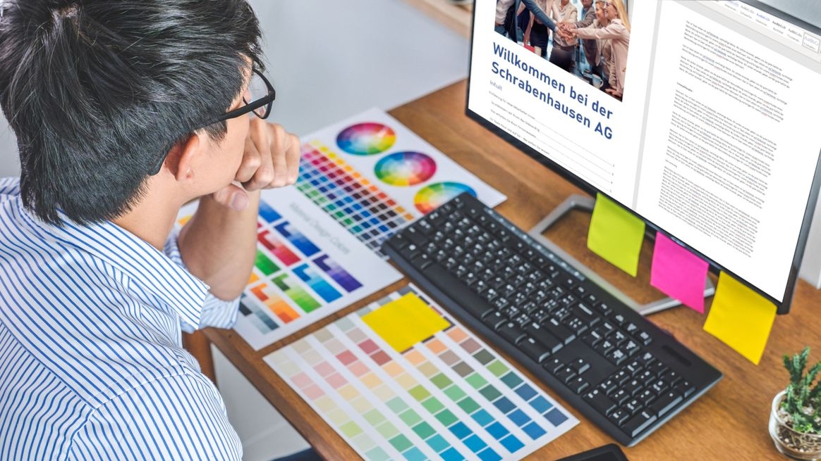  Person sitzt vor einem Computerbildschirm mit Inhaltsverzeichnis, auf dem Schreibtisch liegen Karten mit Farbvorschlägen