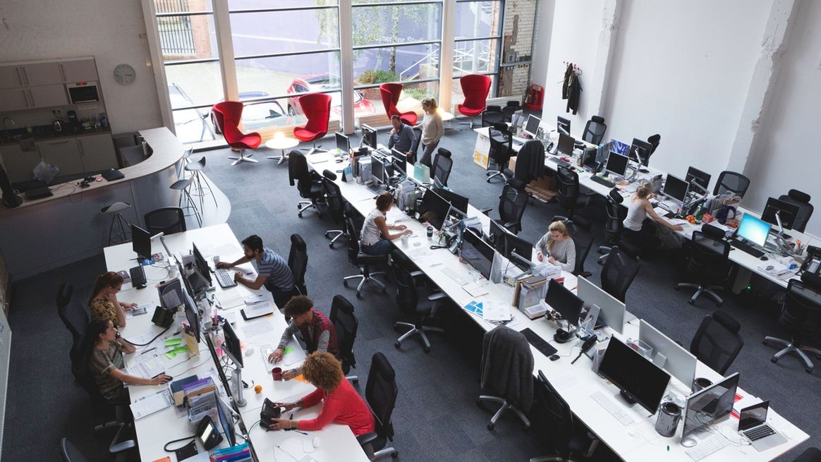 Ansicht von schräg oben auf ein Großraumbüro mit einigen Menschen an Schreibtischarbeitsplätzen