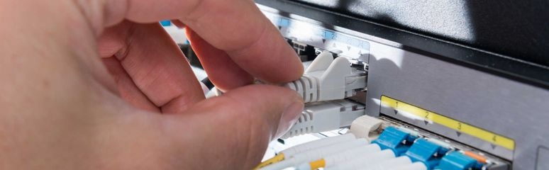 Eine Hand, die den Stecker eines Netzwerkkabels an einem Server-Rack anschließt.