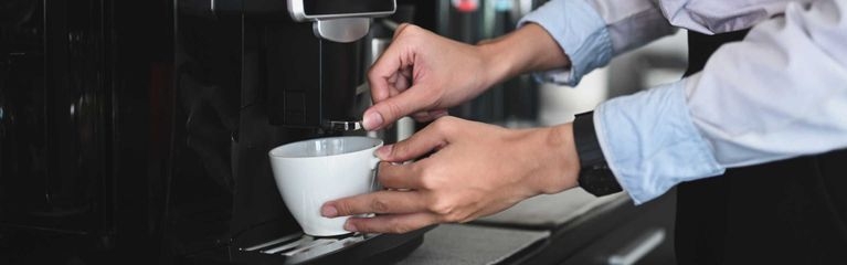 Eine Frau steht vor einem Kaffeevollautomat und füllt sich eine Tasse ab