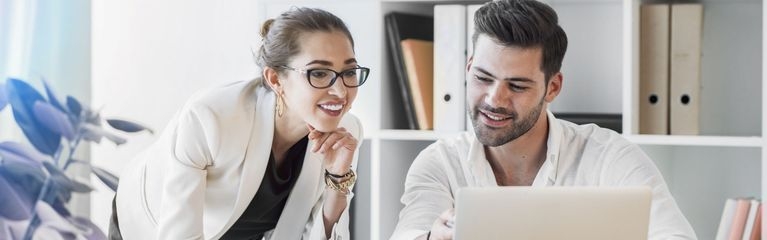 Zwei Menschen sitzen an einem Tisch und schauen nach vorne auf ein Notebook