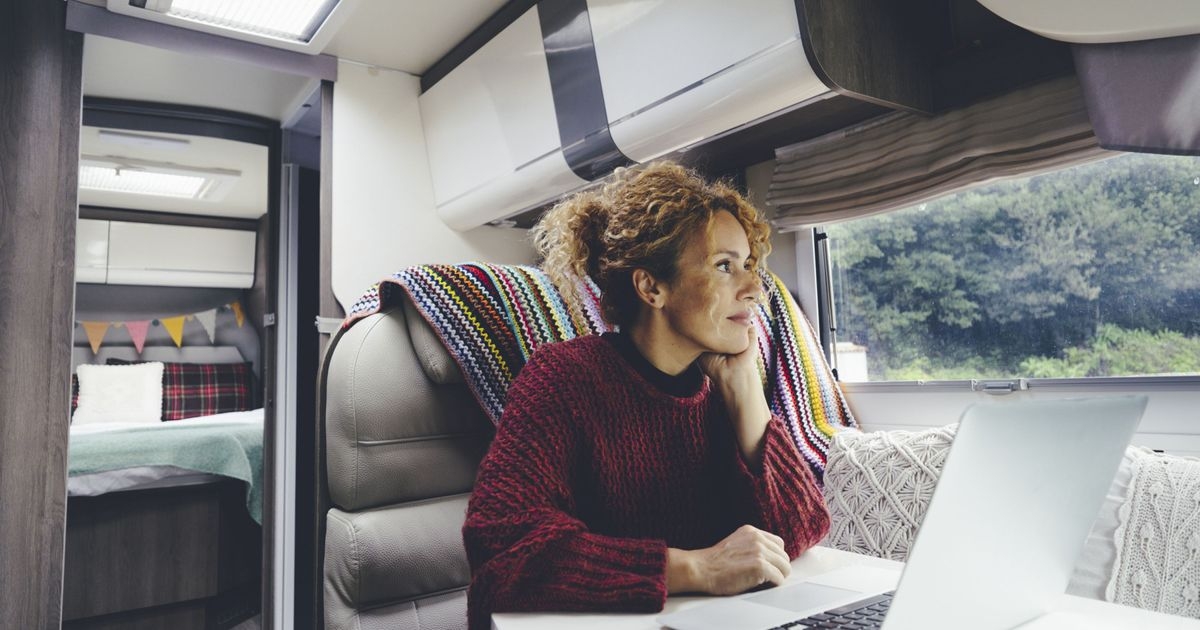 Eine Frau sitzt mit ihrem Notebook an einem Tisch in einem Reisemobil und schaut aus dem Fenster. 