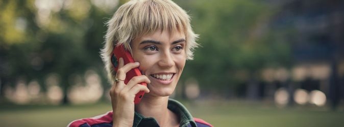 Eine junge Frau telefoniert lächelnd mit einem roten Smartphone