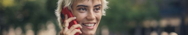 Eine junge Frau telefoniert lächelnd mit einem roten Smartphone