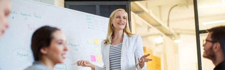 Eine Frau steht vor einem Whiteboard und hält einen Vortrag vor Publikum