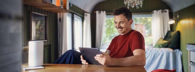 Ein Mann im roten Shirt blickt lächelnd auf ein Tablet