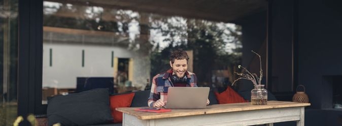 Ein Mann sitzt an einem Schreibtisch und blickt auf den Bildschirm eines Laptops.