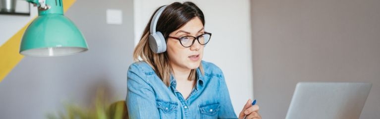 Eine Frau sitzt vor einem Notebook und hält einen Kugelschreiber in der Hand.