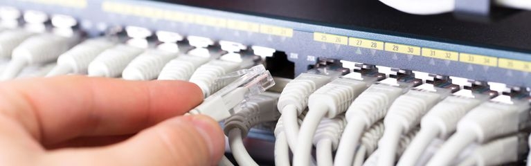 Die Hand eines IT-Technikers verbindet einen Ethernetstecker mit der Buchse in einem Rack 