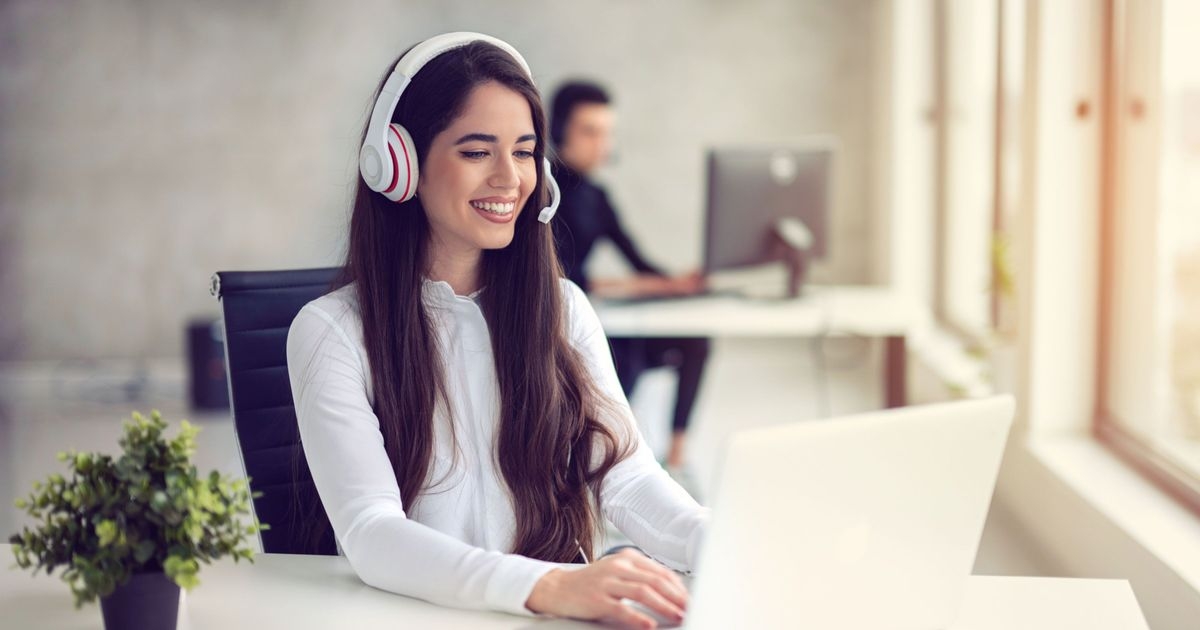 Eine Person mit Headset sitzt vor ihrem Laptop und telefoniert über das Internet.