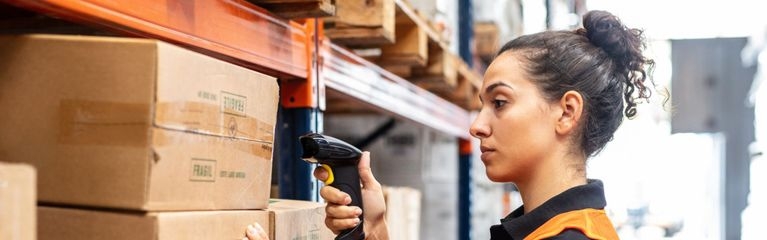 Eine Frau steht vor einem Hochregal und hält einen Handscanner vor ein Paket